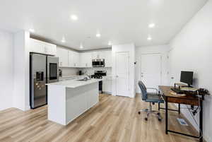 Kitchen with white cabinetry, appliances with stainless steel finishes, a desk, a kitchen island with sink, and light wood finished floors