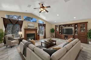 Living room with lofted ceiling, gas fireplace, light marble finish floors, recessed lighting, and a ceiling fan