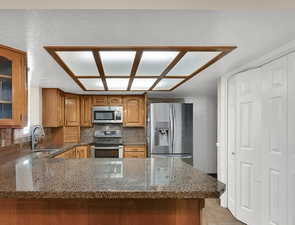 Kitchen featuring dark stone counters, a peninsula, stainless steel appliances, brown cabinetry, and decorative backsplash