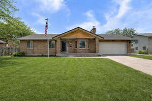 Ranch-style home with a porch, brick siding, a garage, concrete driveway, and a chimney