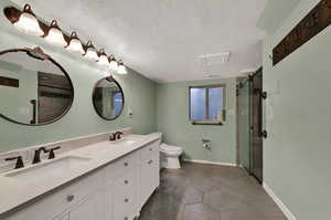 Full bathroom in basement featuring a textured ceiling, double vanity, a shower stall, and dark tile patterned flooring