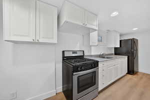 Kitchen with stainless steel gas range oven, white cabinetry, light countertops, light wood-type flooring, and recessed lighting