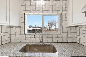 Kitchen view of white cabinetry, light stone counters, extractor fan, and tasteful backsplash