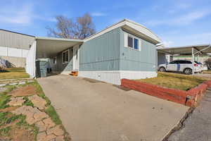 View of side of home featuring an attached carport, concrete driveway, and a yard
