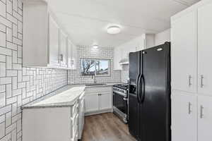 Kitchen with black fridge, white cabinets, stainless steel gas stove, light wood-style flooring, and decorative backsplash