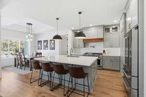 Kitchen with hanging light fixtures, a center island with sink, high end appliances, gray cabinetry, and a raised ceiling