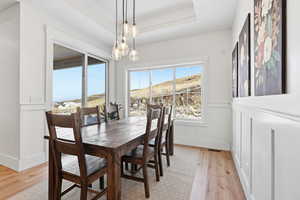 Dining space with light wood finished floors, wainscoting, a tray ceiling, and a decorative wall