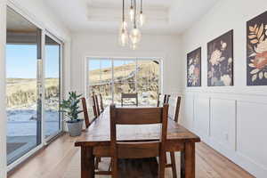 Dining room featuring a decorative wall, a chandelier, a wainscoted wall, light wood-type flooring, and a tray ceiling