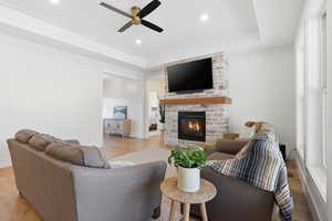 Living room featuring light wood finished floors, a fireplace, a ceiling fan, a raised ceiling, and recessed lighting