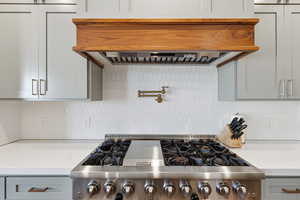 Kitchen view of range hood, pot filler, stainless steel gas range, and tasteful backsplash