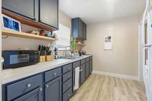 Upstairs Kitchen with blue cabinetry, light countertops, light wood-type flooring, open shelves, and black microwave