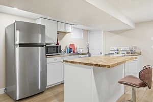 Downstairs Kitchen with wood counters, stainless steel appliances, white cabinets, light wood-style flooring, and a center island