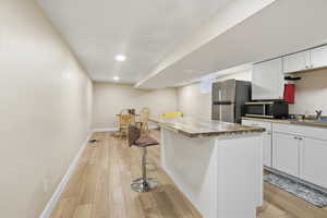 Downstairs Kitchen with a breakfast bar area, white cabinetry, light wood finished floors, a kitchen island, and appliances with stainless steel finishes