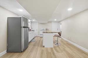 Downstairs Kitchen featuring white cabinets, freestanding refrigerator, a kitchen breakfast bar, electric range, and light wood-style floors