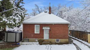 Snow covered house featuring brick siding, a storage shed, and a chimney