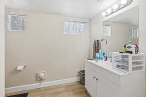 Downstairs bathroom with vanity, light wood-type flooring, and a textured ceiling
