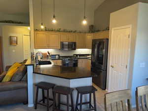 Kitchen with stainless steel appliances, a peninsula, pendant lighting, dark stone counters, and a breakfast bar