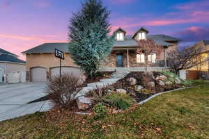 View of front of property with stone siding, covered porch, concrete driveway, and roof with shingles
