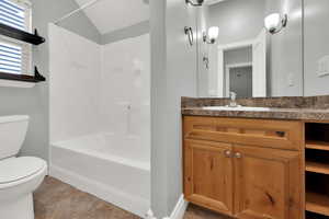 Bathroom with vanity, washtub / shower combination, light tile patterned flooring, and vaulted ceiling