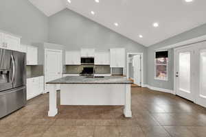 Kitchen with appliances with stainless steel finishes, a kitchen bar, high vaulted ceiling, dark stone counters, and white cabinets