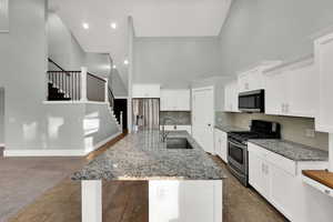 Kitchen with high vaulted ceiling, stainless steel appliances, light stone counters, white cabinets, and tasteful backsplash