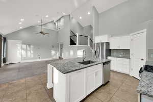 Kitchen featuring high vaulted ceiling, dark stone countertops, white cabinetry, recessed lighting, and an island with sink