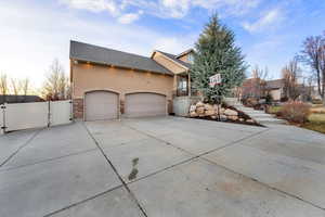 View of home's exterior with a gate, driveway, stone siding, a shingled roof, and stucco siding