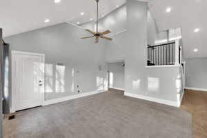Unfurnished living room featuring recessed lighting, ceiling fan, high vaulted ceiling, stairway, and light carpet