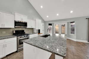 Kitchen with appliances with stainless steel finishes, light stone counters, an island with sink, recessed lighting, and high vaulted ceiling