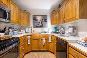 Kitchen with light countertops, stainless steel microwave, gas range oven, black dishwasher, and brown cabinetry