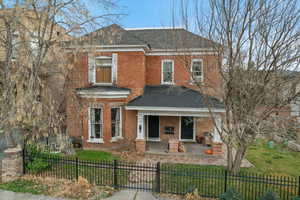 View of front of property featuring covered porch, a fenced front yard, roof with shingles, and brick siding