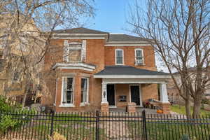 View of front of house featuring a porch, brick siding, a fenced front yard, and roof with shingles