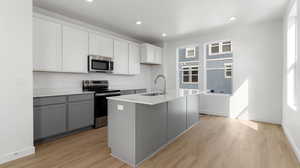 Kitchen with stainless steel appliances, gray cabinets, a kitchen island with sink, light wood-type flooring, and recessed lighting