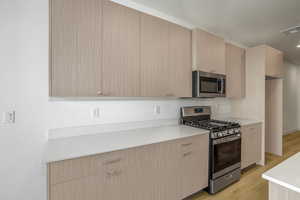 Kitchen featuring light brown cabinetry, appliances with stainless steel finishes, modern cabinets, light wood-style flooring, and light stone counters