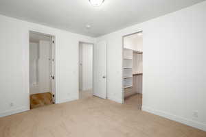 Unfurnished bedroom with light carpet, a spacious closet, and ensuite bath