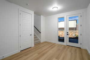 Unfurnished room featuring stairs, light wood-style flooring, a textured ceiling, and french doors