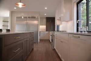 Kitchen with high end appliances, white cabinets, dark wood-type flooring, glass insert cabinets, and decorative backsplash