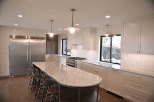 Kitchen with premium appliances, light stone counters, hanging light fixtures, white cabinets, and recessed lighting