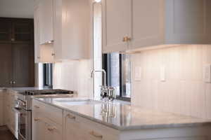 Kitchen with high end stove, decorative backsplash, light stone counters, and white cabinets
