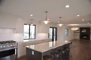 Kitchen with stainless steel gas range oven, white cabinets, decorative backsplash, dark wood finished floors, and recessed lighting