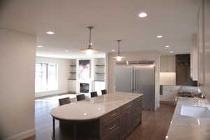 Kitchen featuring light stone countertops, appliances with stainless steel finishes, hanging light fixtures, a kitchen breakfast bar, and a glass covered fireplace