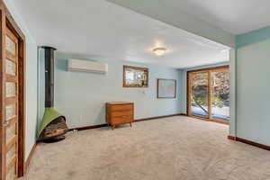 Carpeted spare room with a wood stove, plenty of natural light, and an AC wall unit
