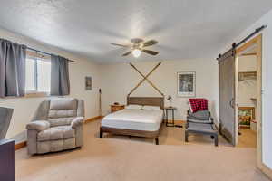 Bedroom with a textured ceiling, carpet flooring, a spacious closet, a barn door, and ceiling fan