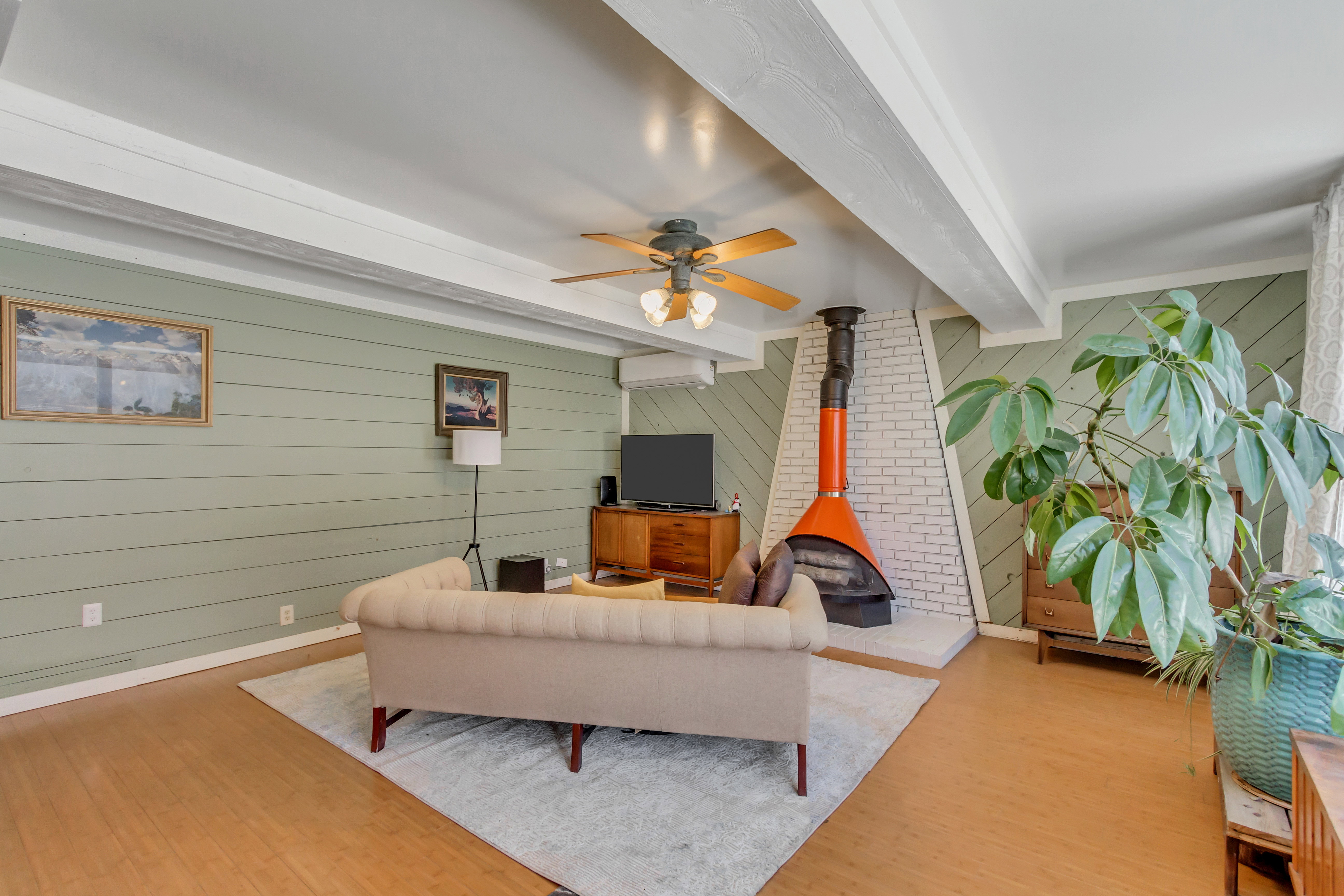 Living room with a wood stove, wood walls, beam ceiling, ceiling fan, and wood finished floors
