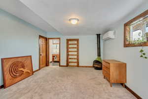 Bedroom featuring a wood stove, light colored carpet, and a wall unit AC