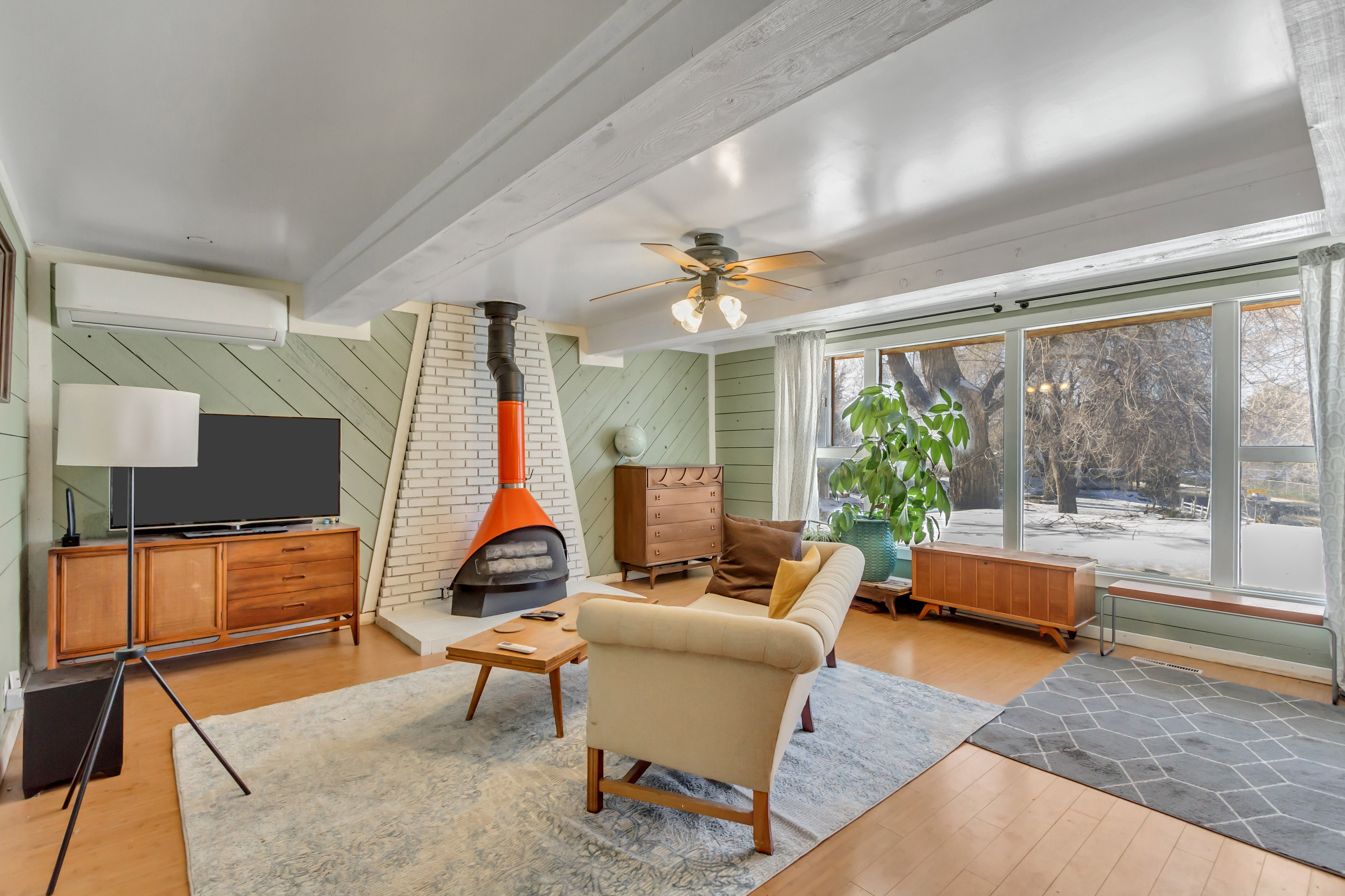Living area featuring a wood stove, ceiling fan, light wood-style flooring, a wall mounted AC, and beamed ceiling
