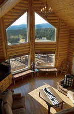 Living area with log walls, dark wood finished floors, a chandelier, wooden ceiling, and high vaulted ceiling