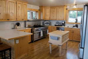 Kitchen with light countertops, stainless steel appliances, light brown cabinets, and a breakfast bar