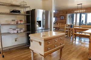 Kitchen featuring stainless steel refrigerator with ice dispenser, light wood finished floors, hanging light fixtures, healthy amount of natural light, and rustic walls