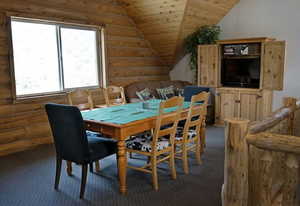 Carpeted dining room featuring wooden ceiling, vaulted ceiling, and rustic walls